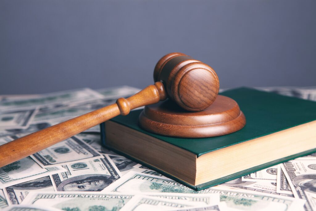 A wooden gavel resting on a book, surrounded by US dollar bills.
